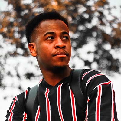 Guy wearing a backpack and wearing a black and ornage striped shirt looing away from the camera.