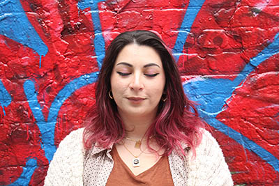 girl with red hair and tan sweater standing in front of bright red spray painted wall